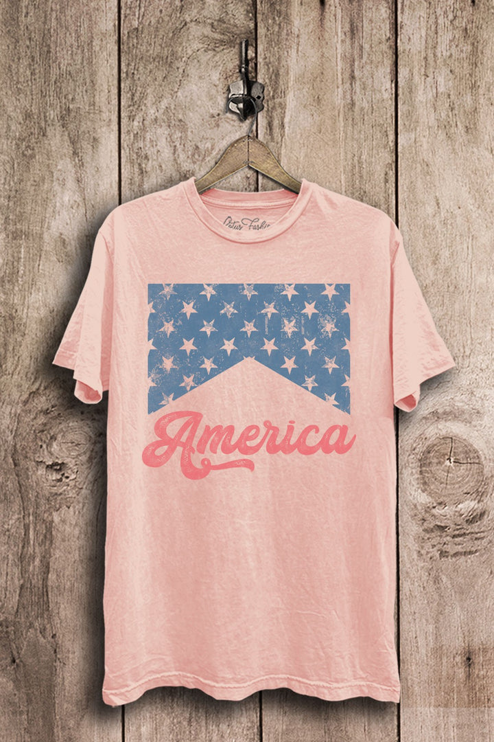 Light pink mineral-washed boyfriend tee featuring a distressed blue star-banner graphic and coral America script lettering.