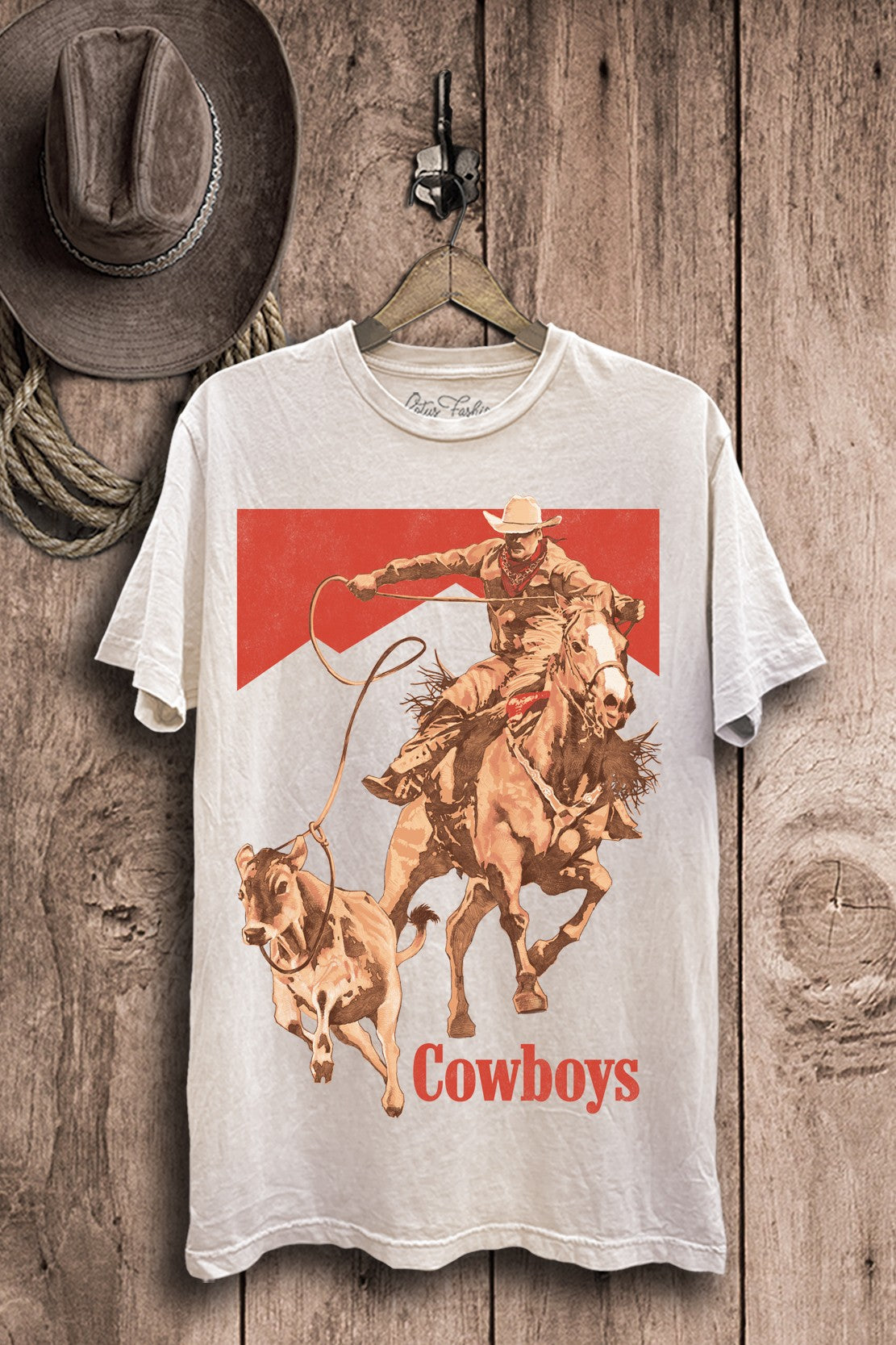 Off-white mineral-wash plus-size boyfriend tee featuring a cowboy on horseback roping cattle with bold red western accents.