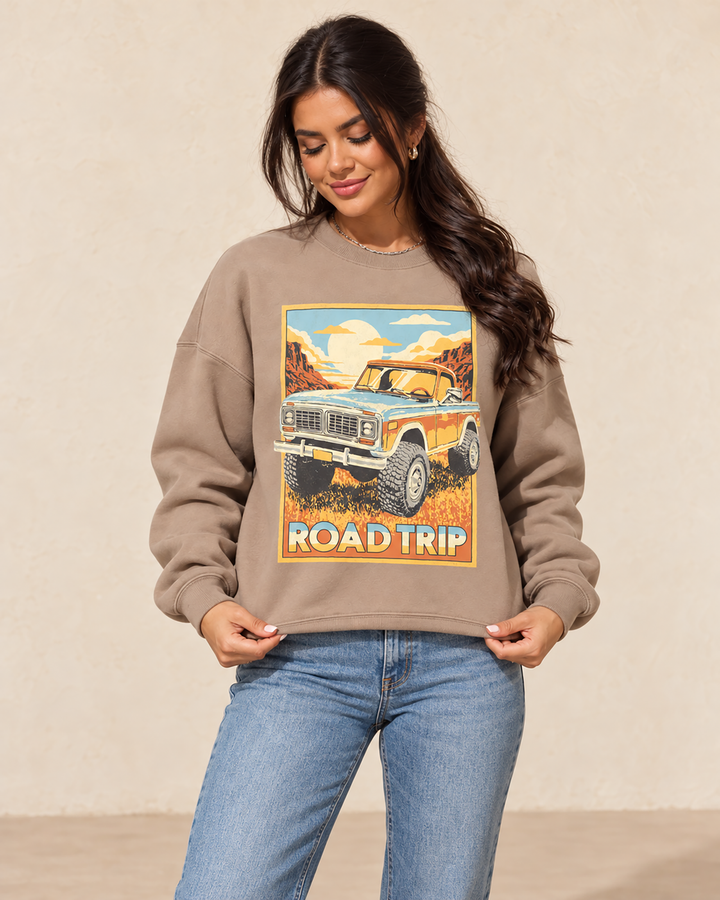 Mocha French terry crewneck sweatshirt featuring a vintage blue and orange off-road truck traveling through a sunlit canyon with Road Trip lettering.