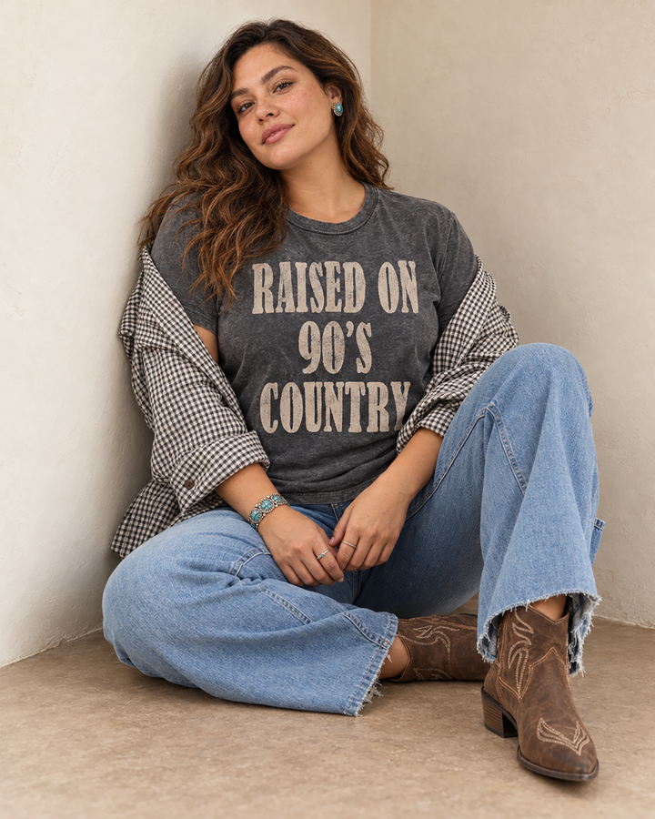 Vintage black mineral-washed boyfriend tee featuring oversized distressed tan lettering that reads Raised on 90s Country.