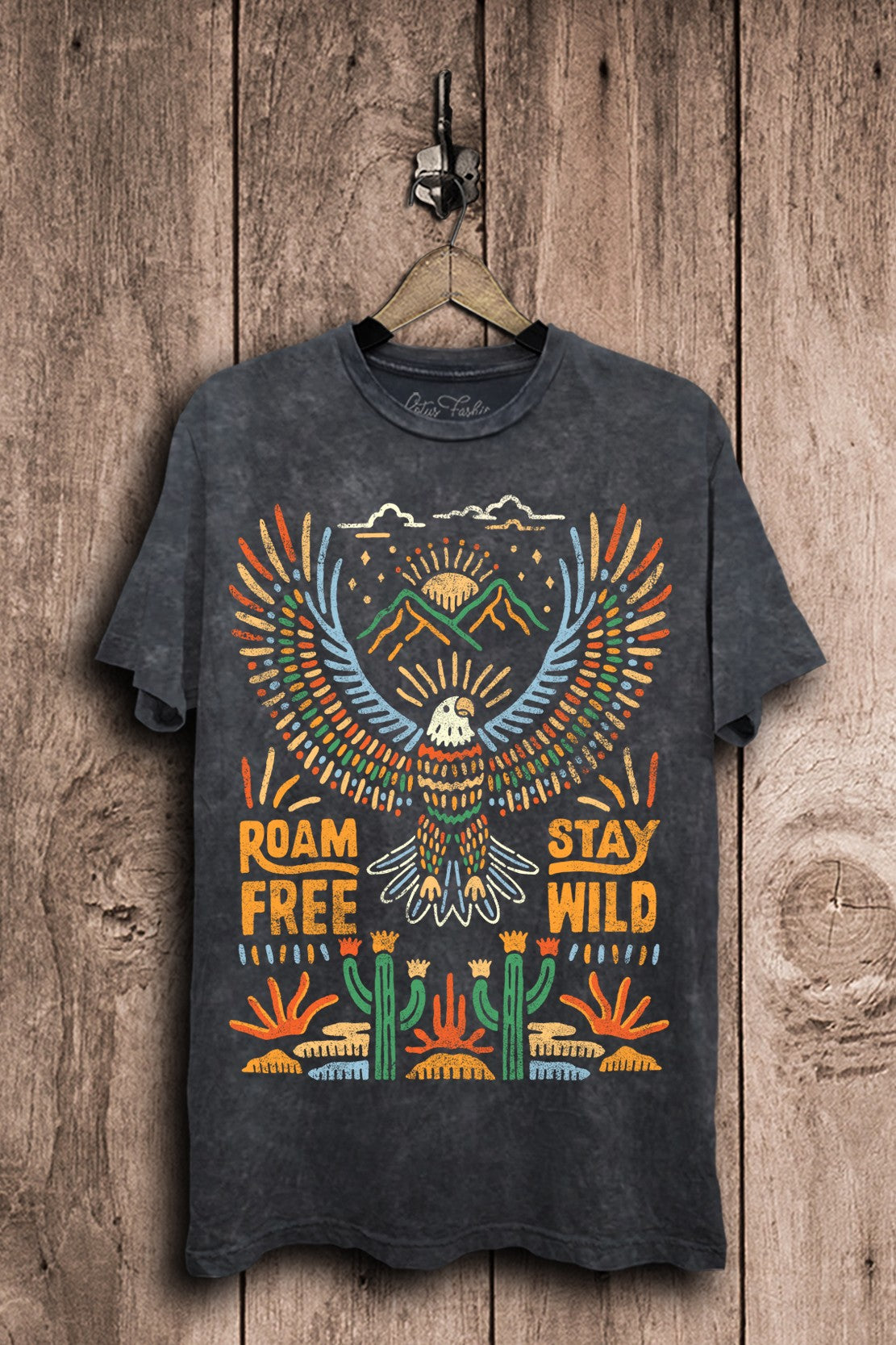 Vintage black mineral-washed boyfriend tee featuring a colorful soaring eagle, mountain peaks, rising suns, desert cacti, and Roam Free Stay Wild lettering.