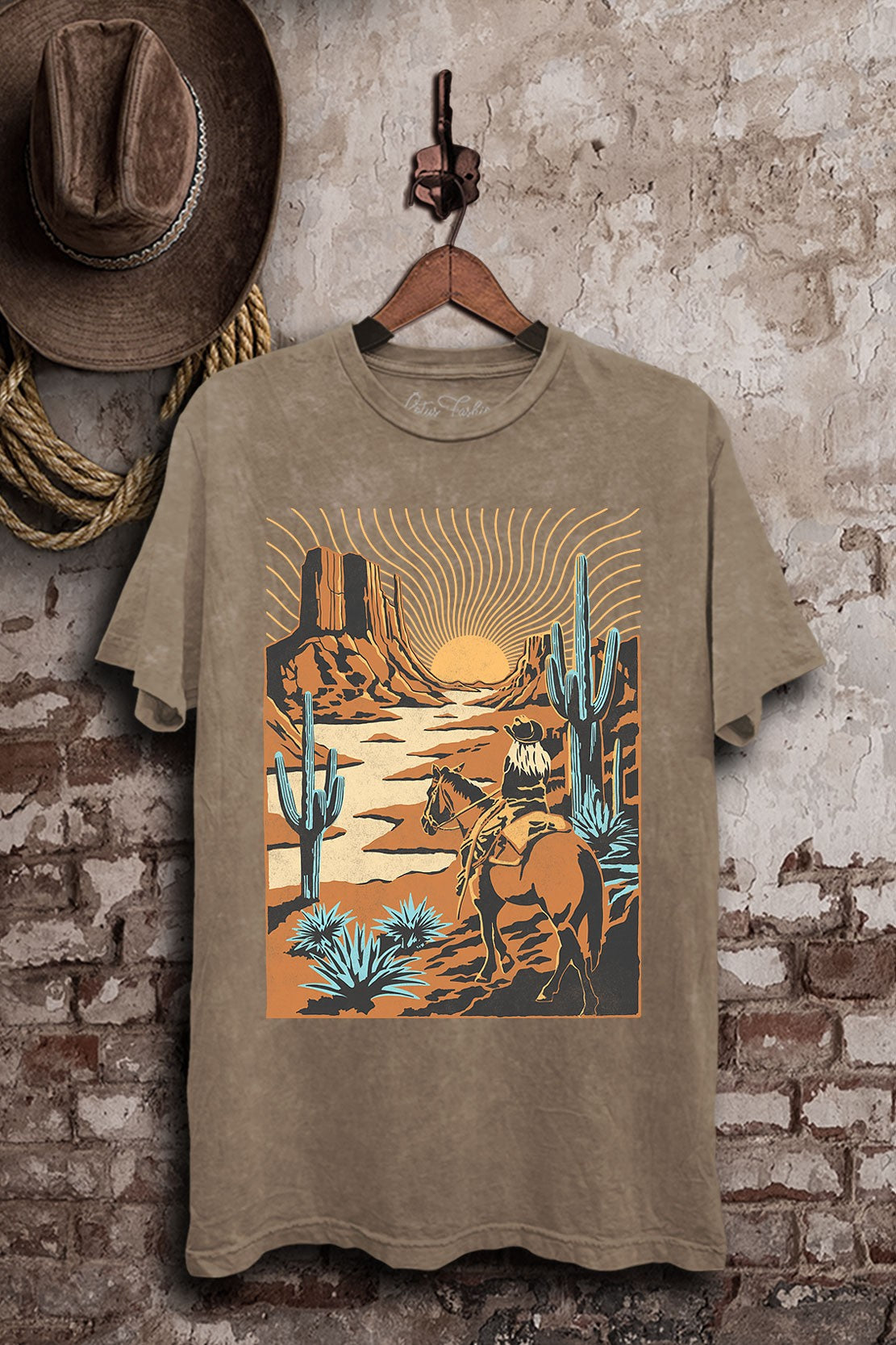 Mocha mineral-washed boyfriend tee featuring a cowboy riding through a sunset desert with mesas, tall cacti, and turquoise-colored plants.