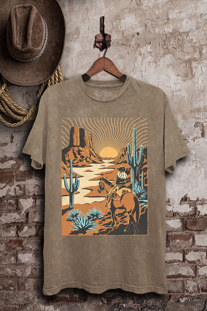 Mocha mineral-washed boyfriend tee featuring a cowboy riding through a sunset desert with mesas, tall cacti, and turquoise-colored plants.