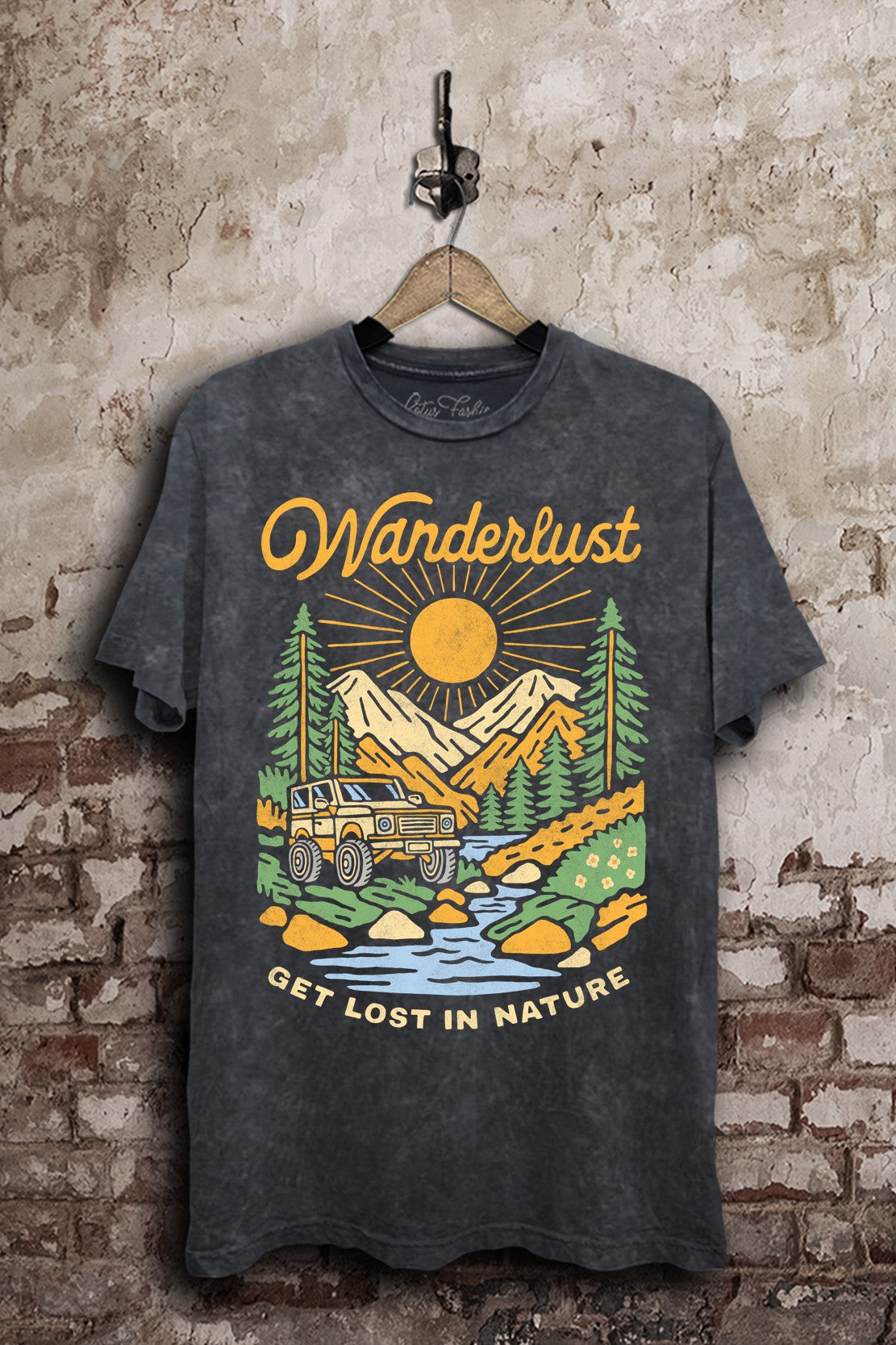 Vintage black mineral-washed boyfriend tee featuring an off-road vehicle, mountain stream, pine trees, wildflowers, and Wanderlust lettering.