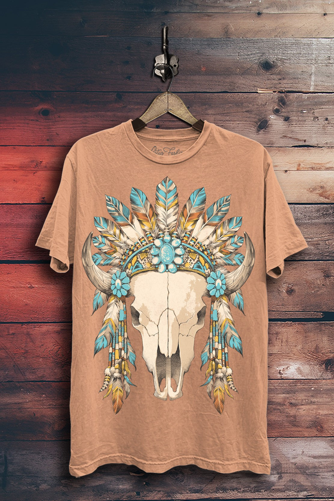 Warm-toned mineral-wash boyfriend tee featuring a cow skull surrounded by turquoise-colored stones, layered feathers, and beaded details.