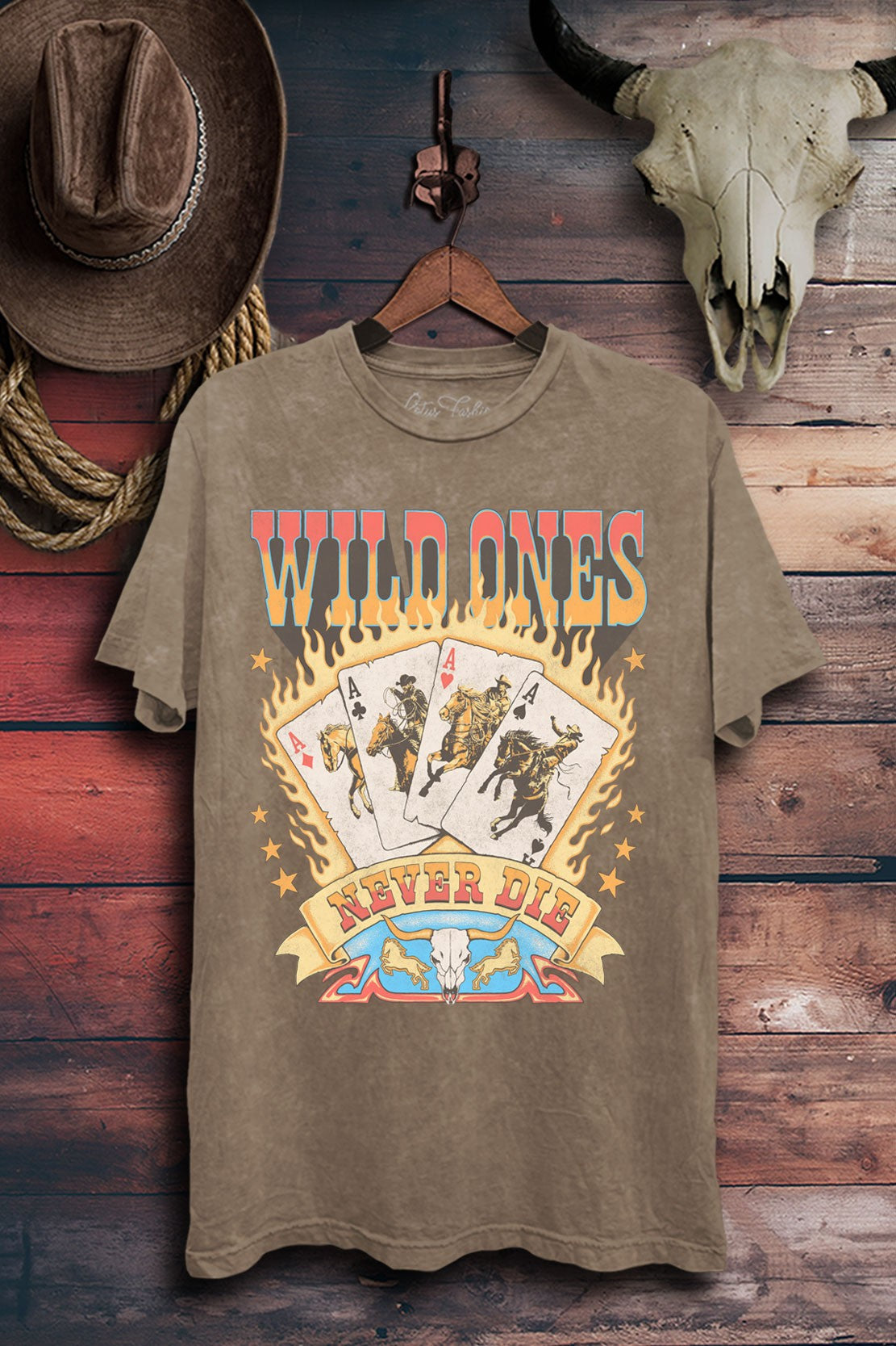 Mocha mineral-wash boyfriend tee featuring Wild Ones Never Die lettering, flaming cowboy playing cards, stars, and a longhorn skull.
